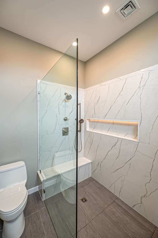 Frameless glass shower with marble tile and built-in bench in Miller Place custom home bathroom
