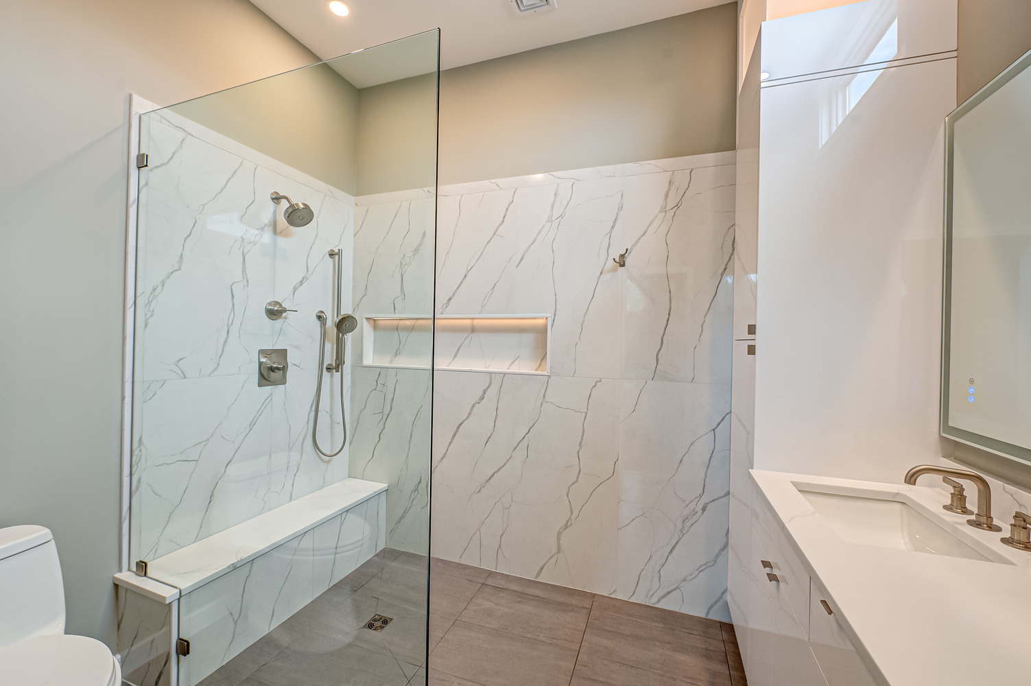 Frameless shower with marble tile and built-in bench in Miller Place custom home by Long Island Creative Contracting