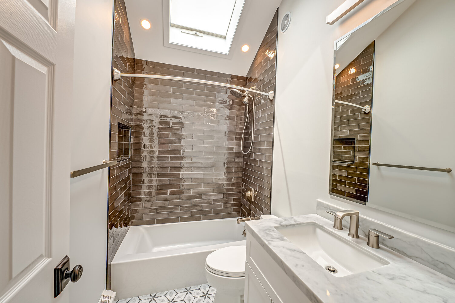 Modern guest bathroom with dark tile shower, marble vanity, and skylight in Huntington, NY custom home