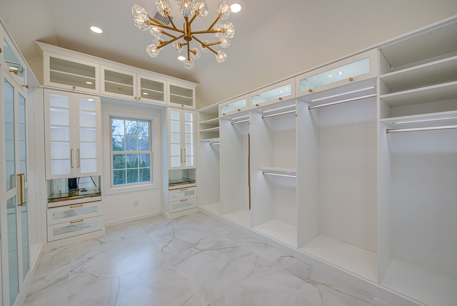 Designer walk-in closet featuring built-in drawers and gold handles in Port Jefferson Station, NY by Long Island Creative Contracting, Inc
