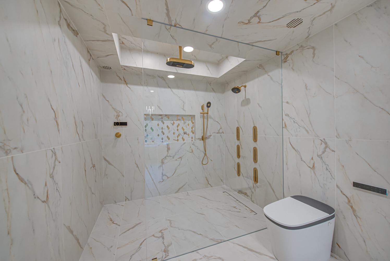 Frameless glass walk-in shower with gold fixtures in custom home by Long Island Creative Contracting, Inc. in Suffolk County, NY