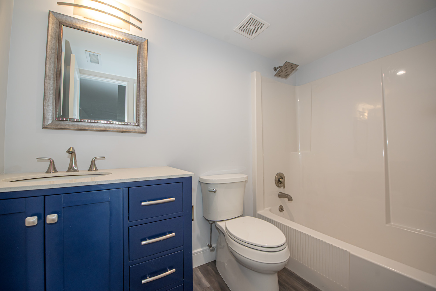 Bathroom remodel with bold navy vanity and sleek fixtures in Port Jefferson, NY by Long Island Creative Contracting, Inc