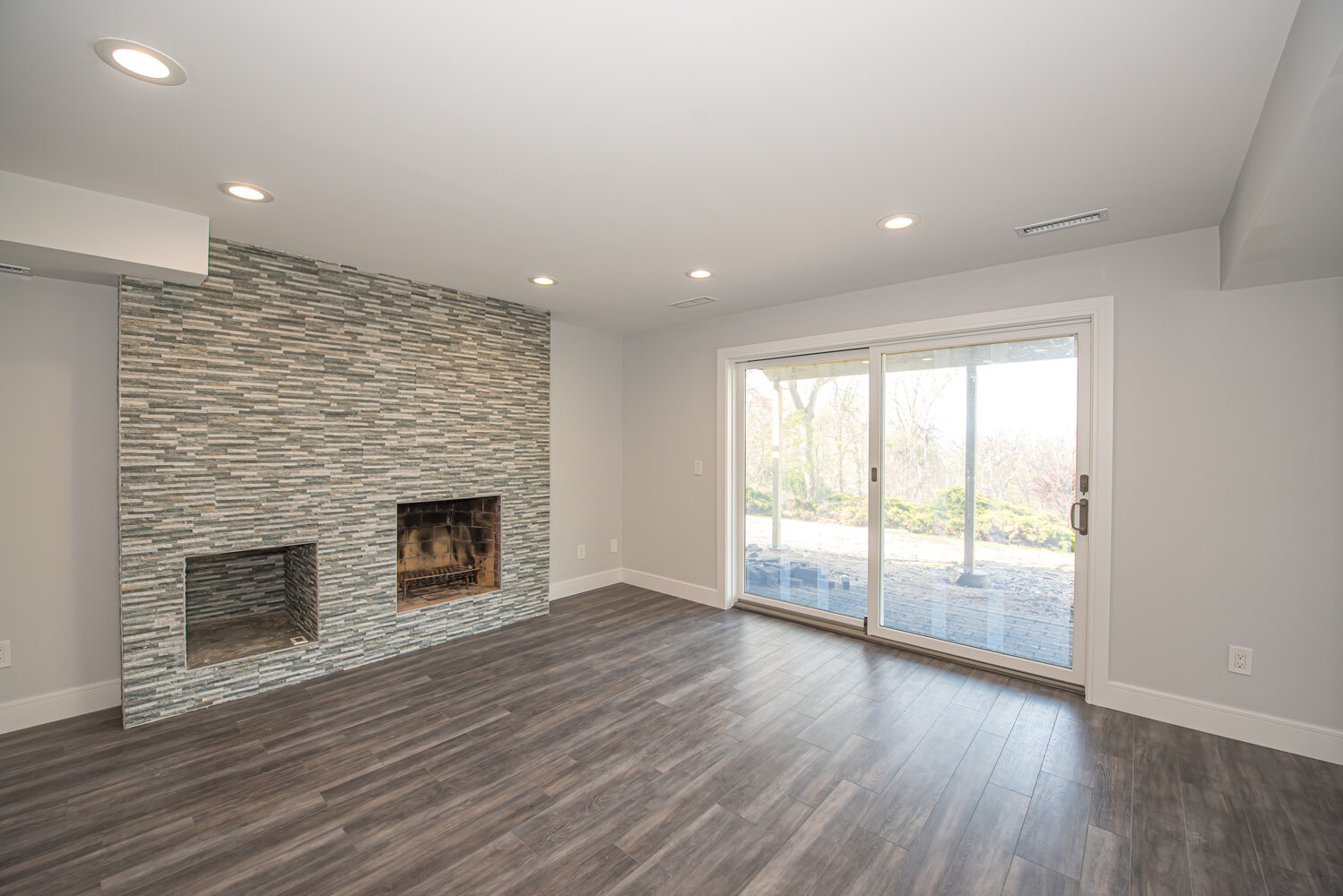 Fireplace feature wall in finished basement with sliding glass doors in Northport, NY custom home