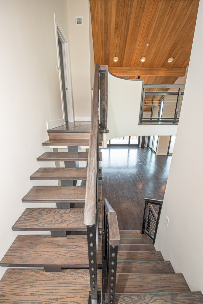 Floating staircase with dark wood treads and custom iron railing in a Miller Place custom home by Long Island Creative Contracting, Inc