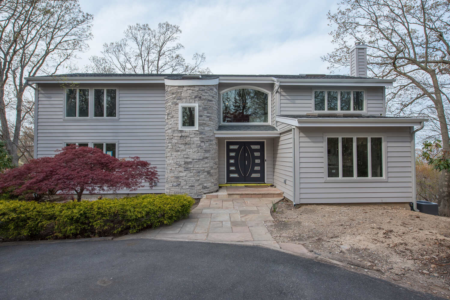 Front exterior of a two-story custom home with gray siding and stone facade in Remsenberg NY by Long Island Creative Contracting, Inc