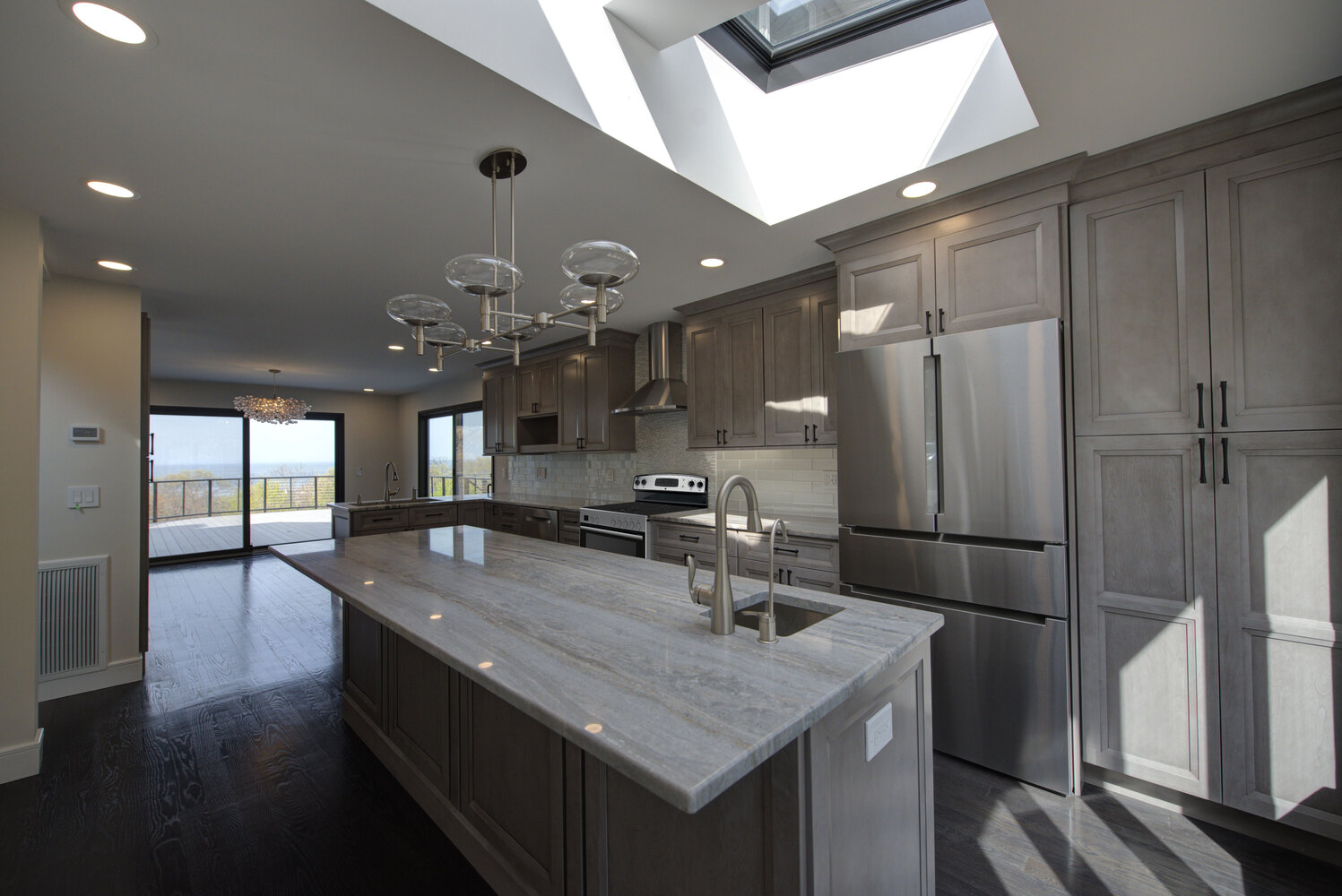 Gourmet kitchen with ocean views and elegant pendant lighting by Long Island Creative Contracting, Inc., Suffolk County, NY