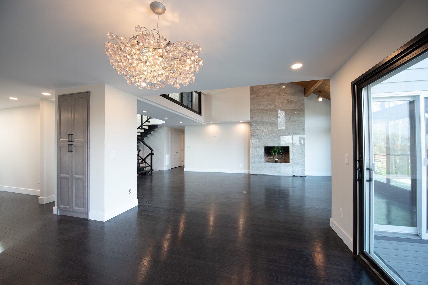 Open concept living space with modern chandelier and floor-to-ceiling fireplace in Port Jefferson, NY by Long Island Creative Contracting, Inc
