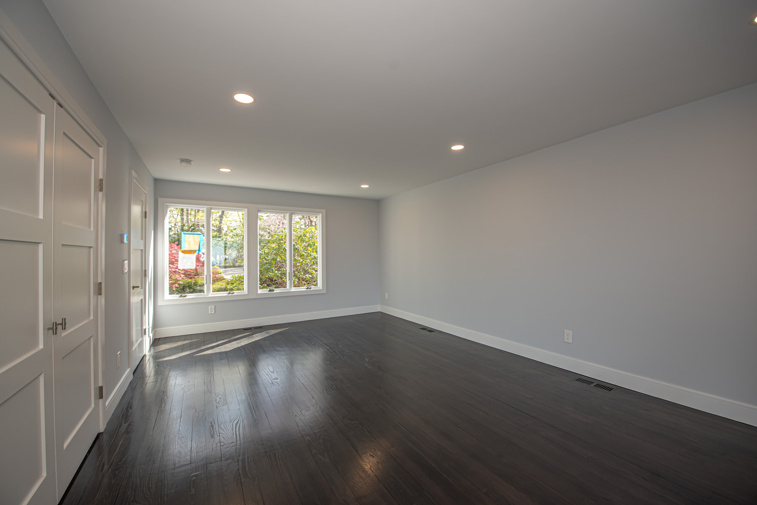 Renovated bedroom with dark wood flooring and large windows in Huntington, NY by Long Island Creative Contracting, Inc