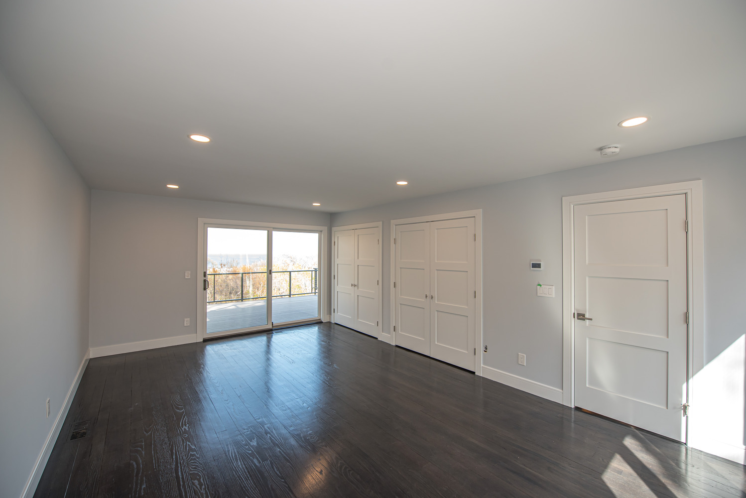 Spacious bedroom with hardwood flooring and sliding door to deck in East Setauket, NY by Long Island Creative Contracting, Inc