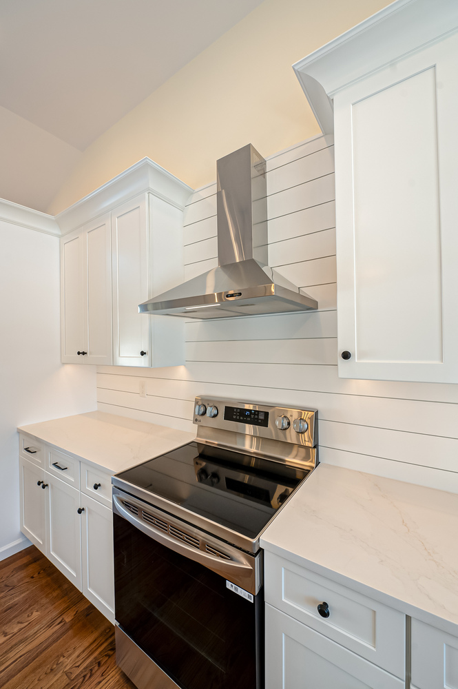 Close-up of stainless steel stove and hood with white shiplap backsplash in a Northport, NY custom home by Long Island Creative Contracting, Inc