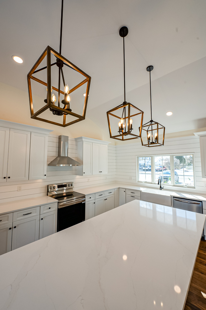 Quartz island and bronze pendant lights in a custom kitchen by Long Island Creative Contracting, Inc. in Port Jefferson, NY