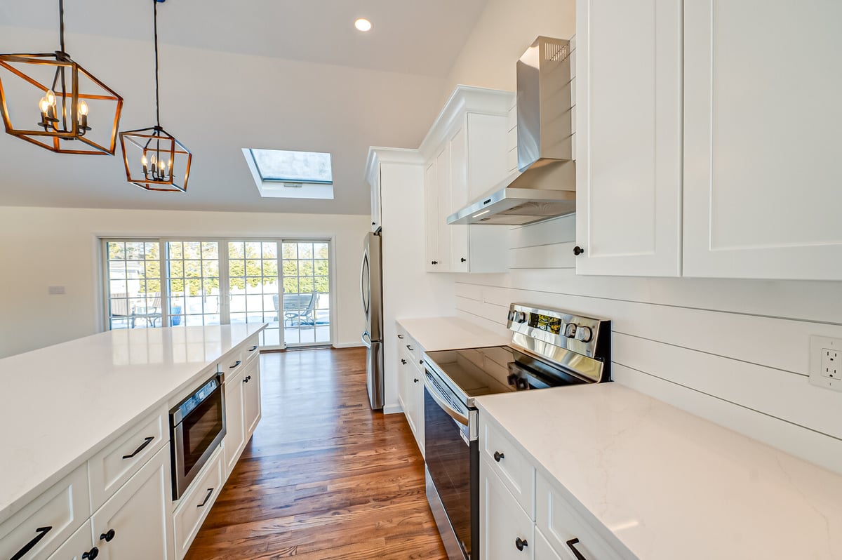 White kitchen with range hood and natural wood floors by Long Island Creative Contracting in Woodbury, NY