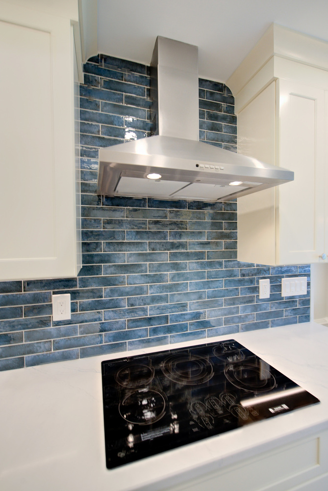 Stainless steel range hood and cooktop with deep blue tile backsplash in a Suffolk County custom kitchen by Long Island Creative Contracting, Inc