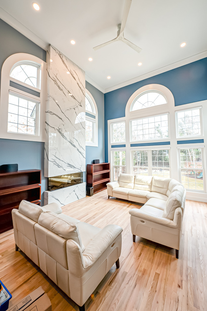 Bright open-concept living room with marble fireplace and arched windows in East Setauket, NY home by Long Island Creative Contracting, Inc