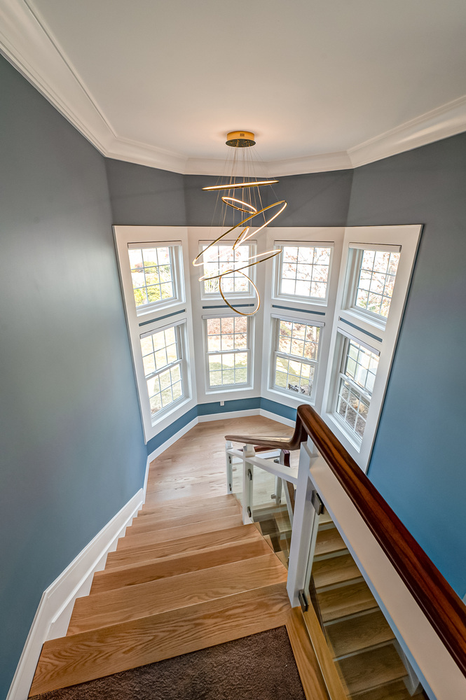 Custom staircase with bay windows and modern chandelier in Suffolk County, NY home by Long Island Creative Contracting, Inc