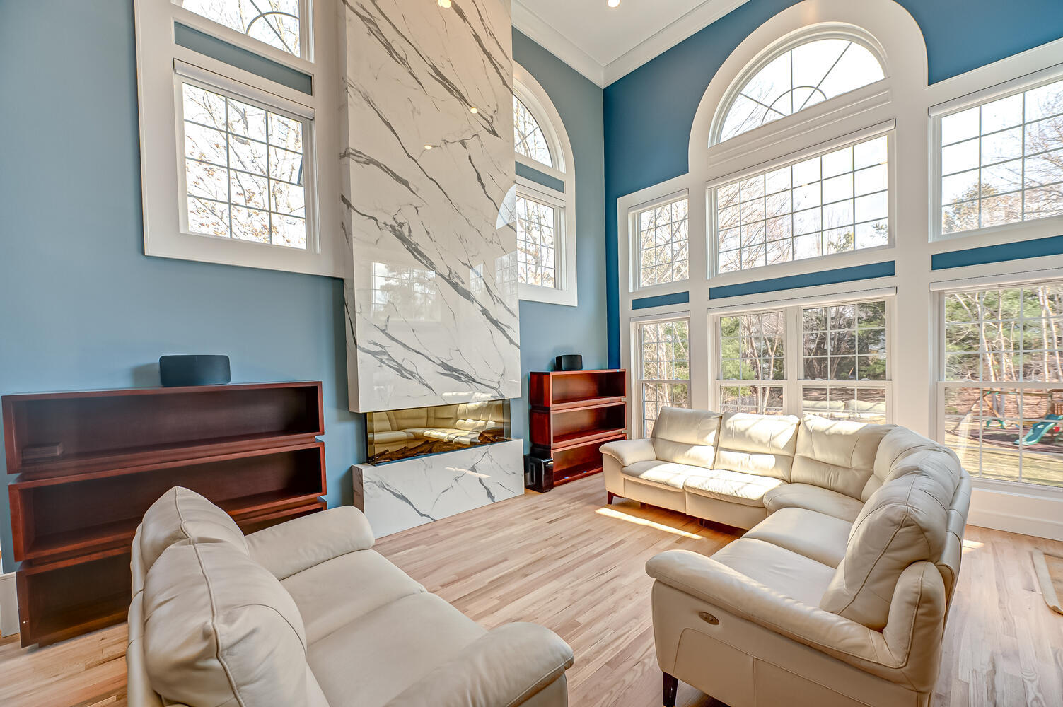 Natural light fills this custom living room with marble fireplace and floor-to-ceiling windows in Old Field, NY home