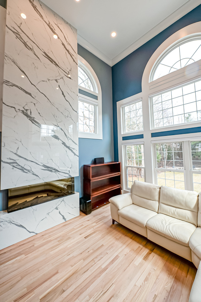 Tall marble fireplace and arched windows in a light-filled custom living room by Long Island Creative Contracting, Inc. in Suffolk County, NY