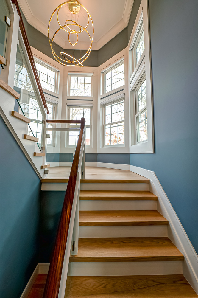 View up stairwell with modern gold chandelier and large windows in Suffolk County home by Long Island Creative Contracting, Inc