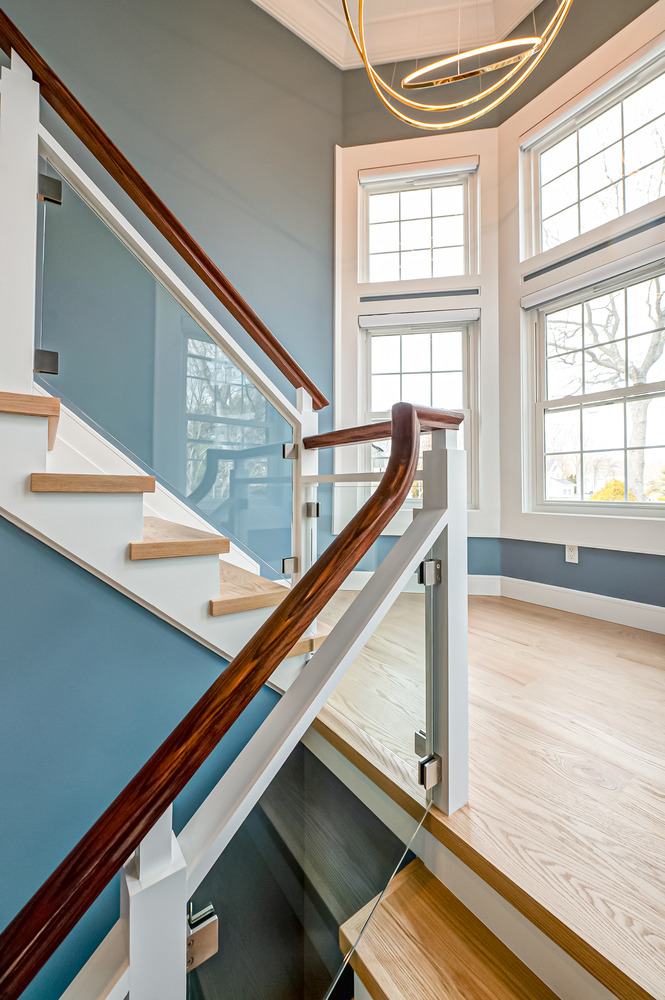 Wood staircase with glass railing and natural lighting in custom Centereach, NY home by Long Island Creative Contracting, Inc