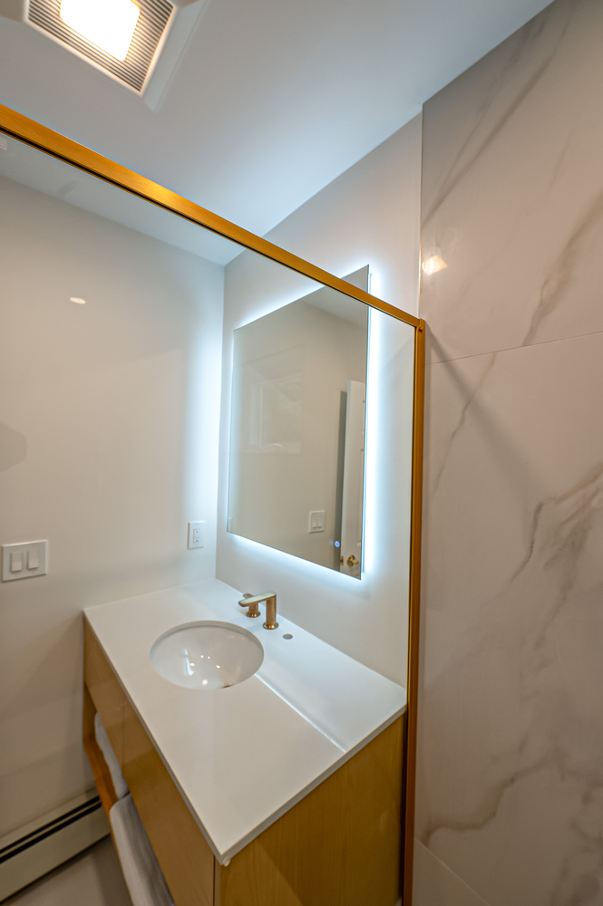 Minimalist bathroom vanity with backlit mirror in a Long Island Creative Contracting custom home in Woodbury, NY