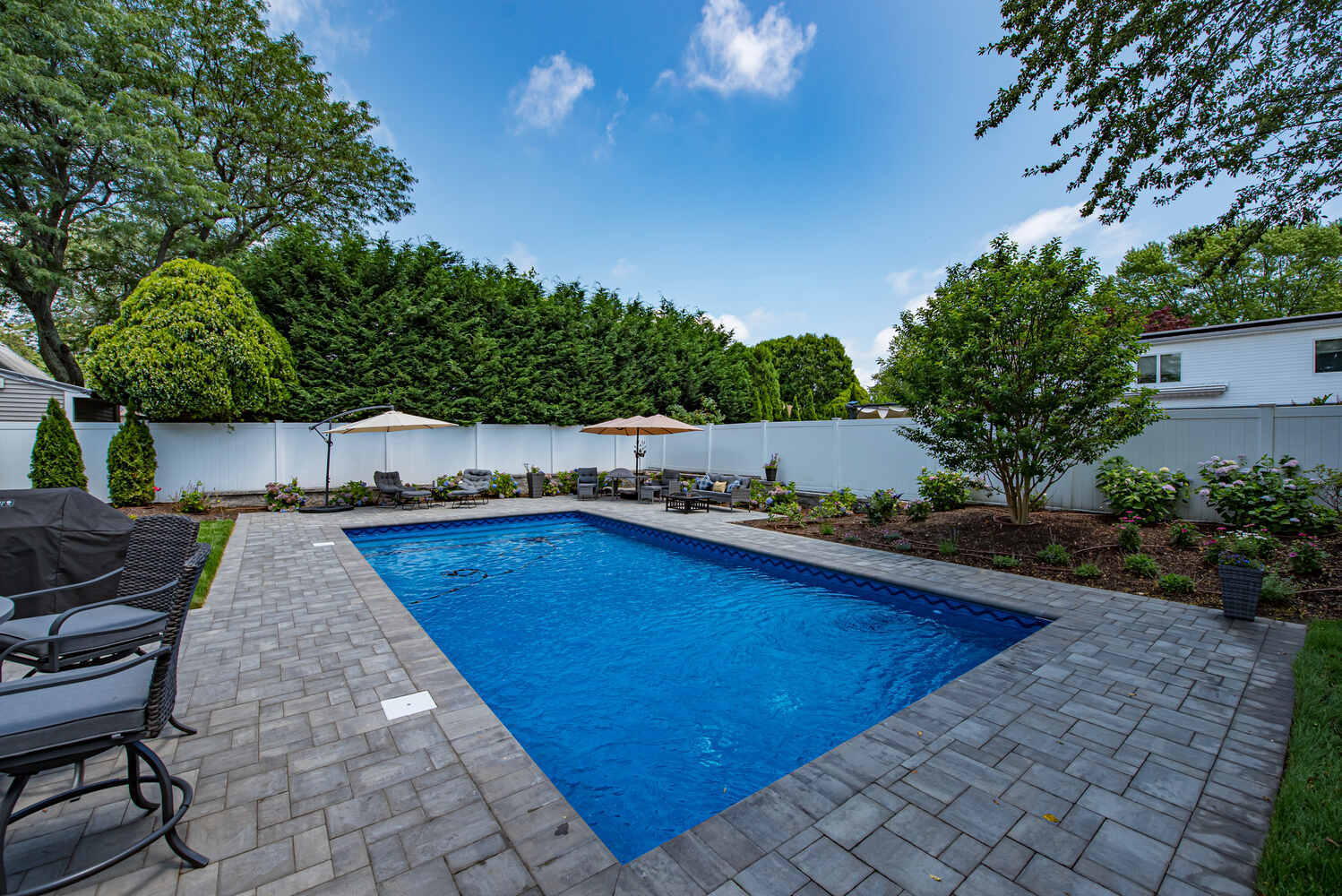 Custom backyard pool surrounded by lush landscaping and lounge seating in Miller Place, NY by Long Island Creative Contracting