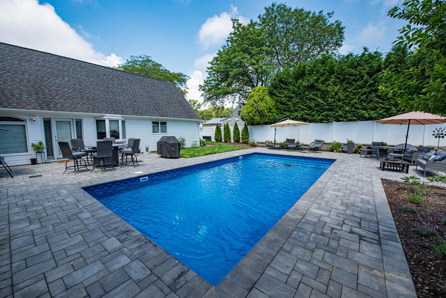 Custom paver patio with pool and lush landscaping by Long Island Creative Contracting, Inc. in Miller Place, NY