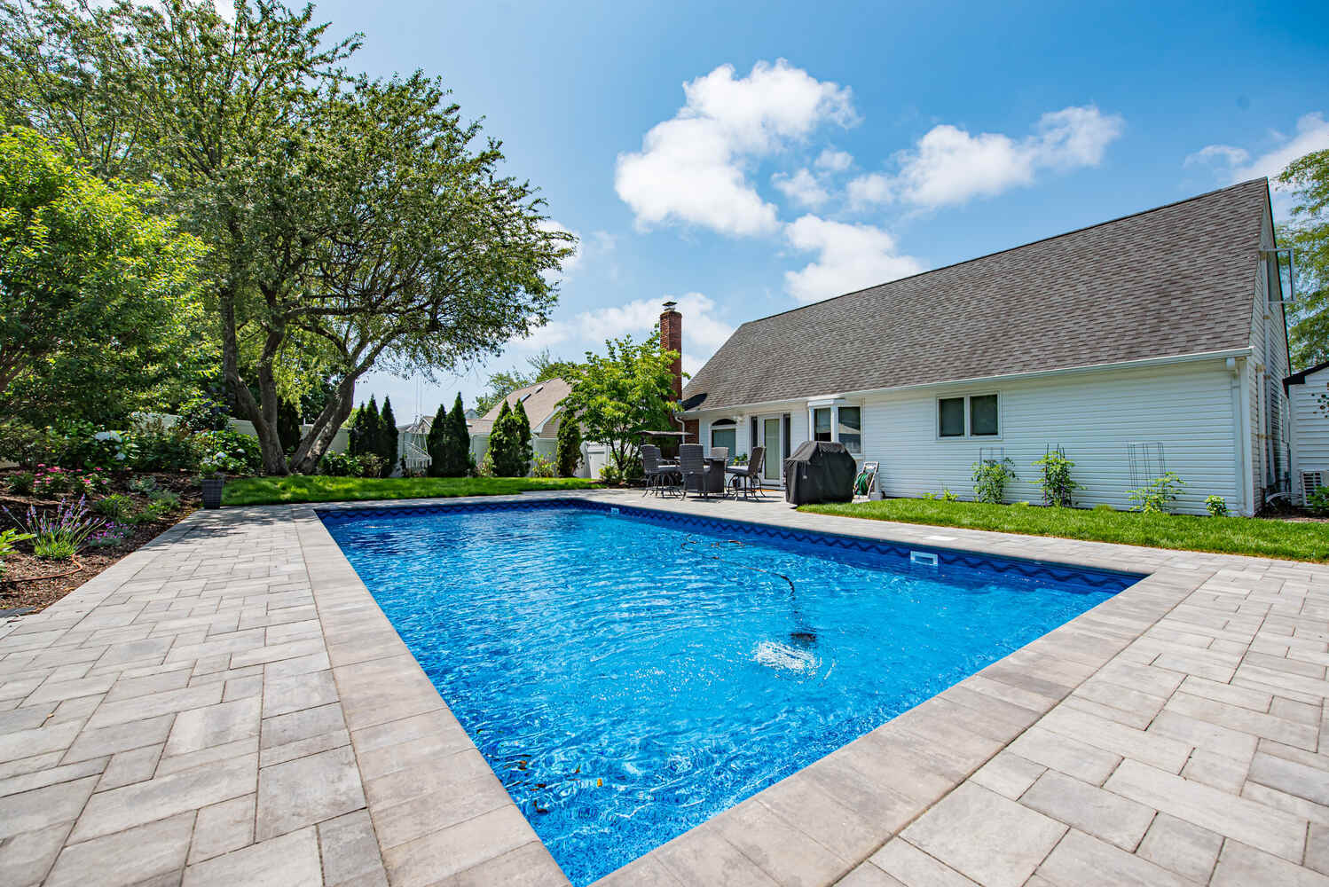 Rear view of modern backyard pool and white home in Miller Place custom build by Long Island Creative Contracting