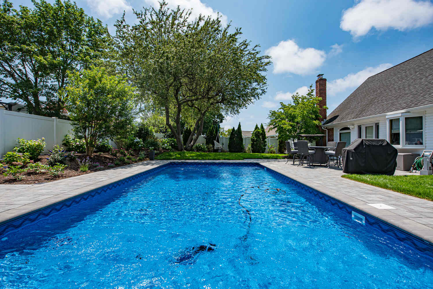 Vibrant custom backyard pool with stone surround by Long Island Creative Contracting in Miller Place, NY