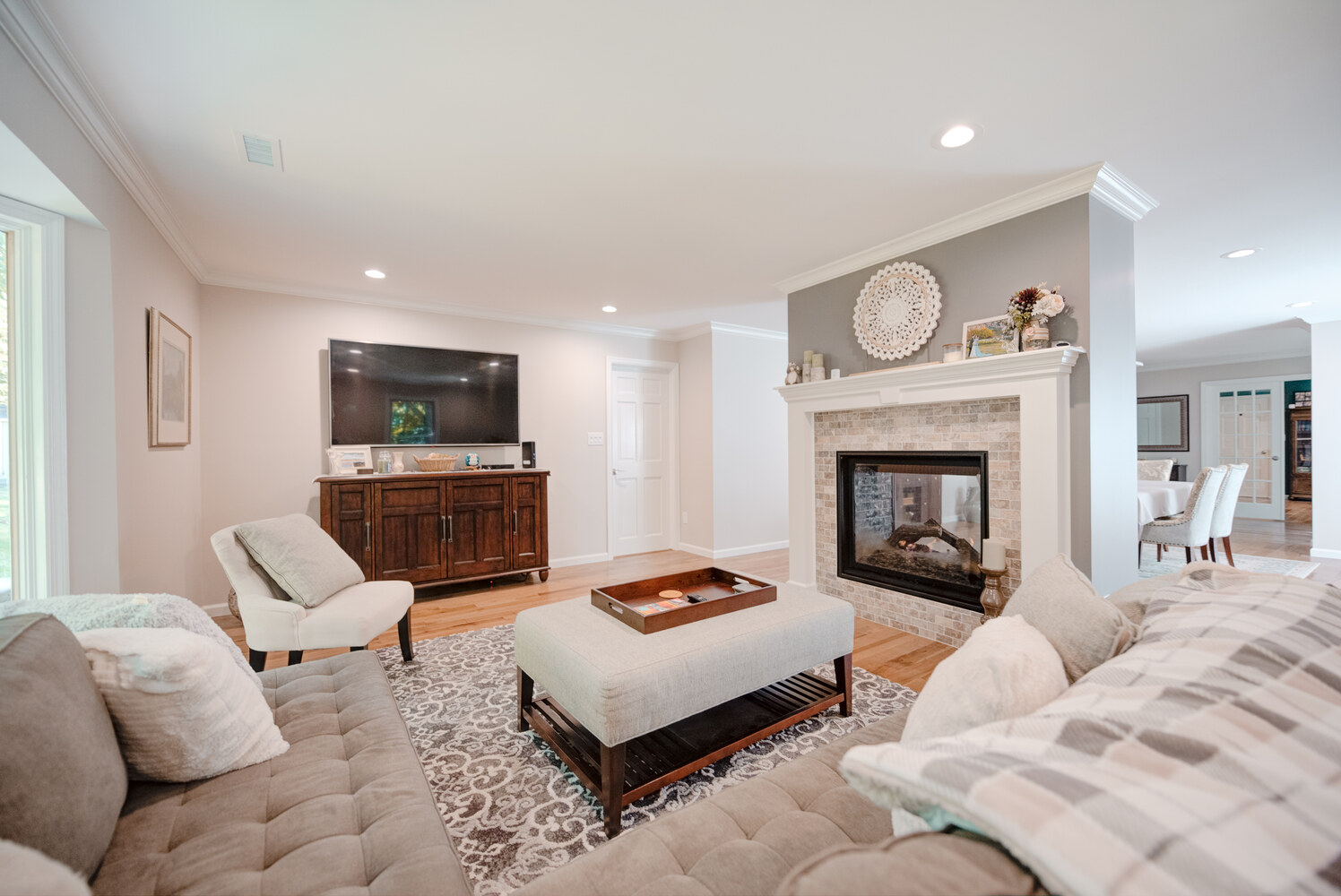 Cozy living room with double-sided fireplace and TV unit in a Suffolk County custom home by Long Island Creative Contracting, Inc.