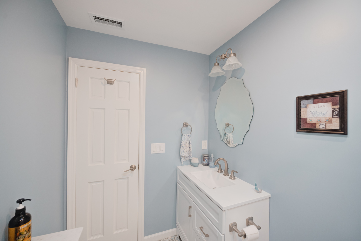 Light blue powder room with framed art and wall-mounted lighting in a Miller Place home by Long Island Creative Contracting