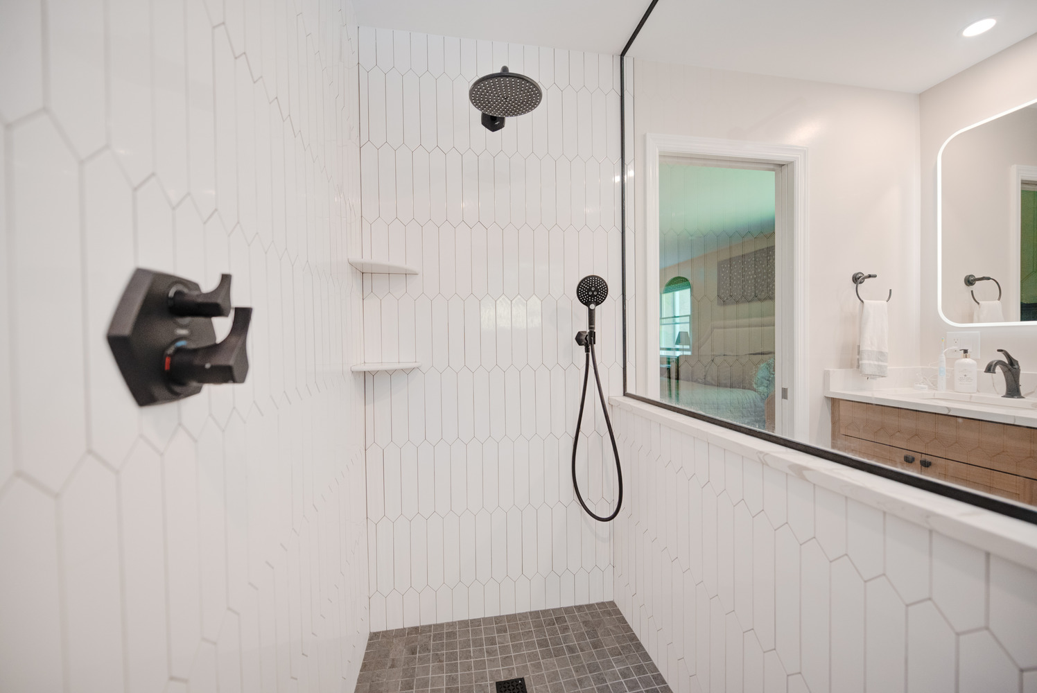 Renovated shower space with dark fixtures and minimalist white tile in Long Island custom home