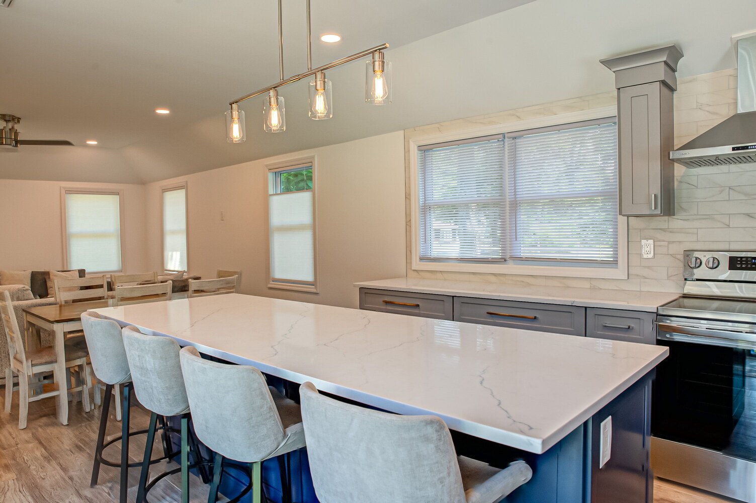 Large island kitchen with gray cabinetry and open dining layout in a new home by Long Island Creative Contracting in East Setauket, NY