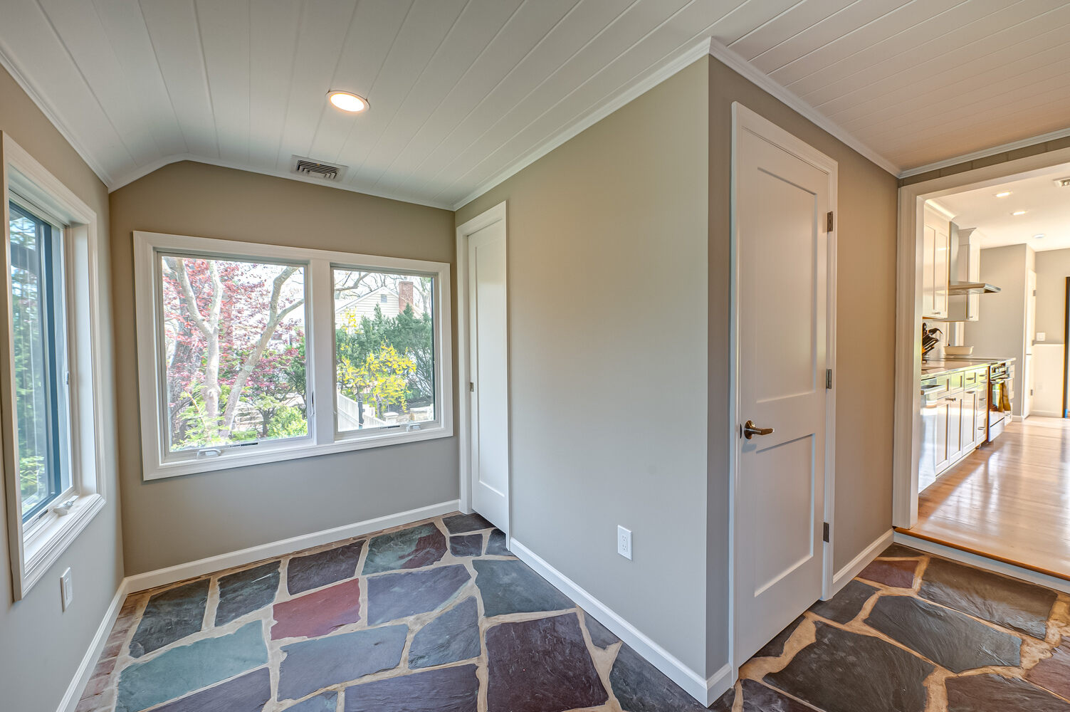 Light-filled corner mudroom with slate flooring and outdoor views in a Miller Place home by Long Island Creative Contracting