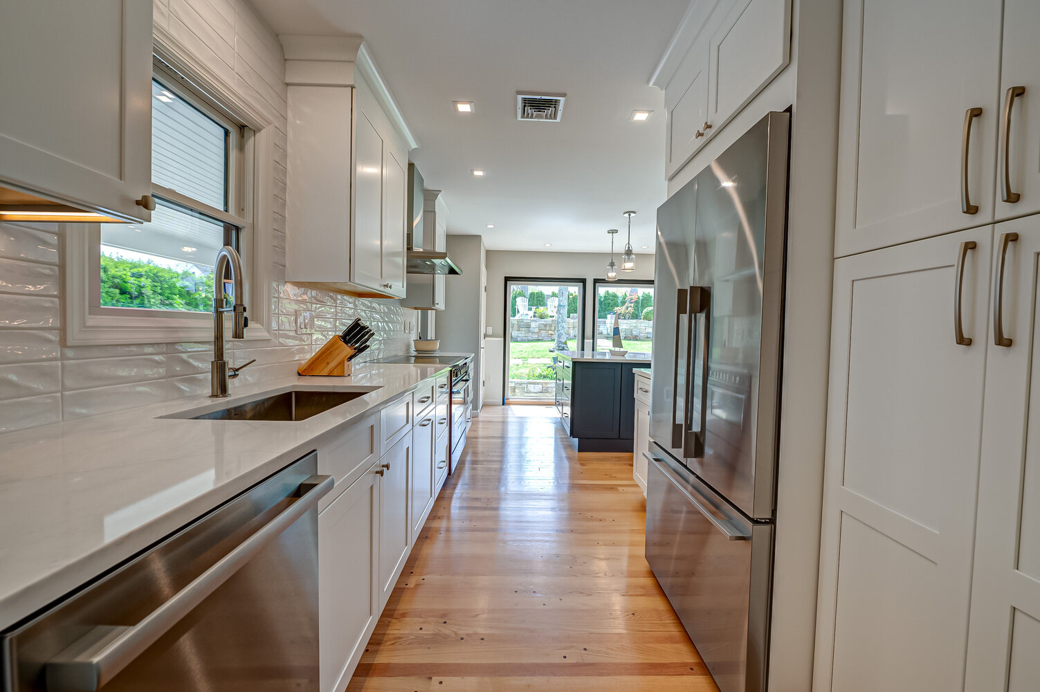 Sleek galley kitchen with white cabinetry and stainless steel appliances by Long Island Creative Contracting in Miller Place, NY