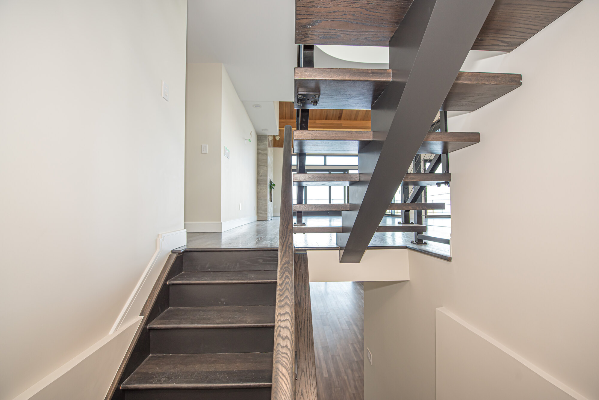 Modern staircase with open wood treads and black railing in Mount Sinai, NY custom home by Long Island Creative Contracting, Inc