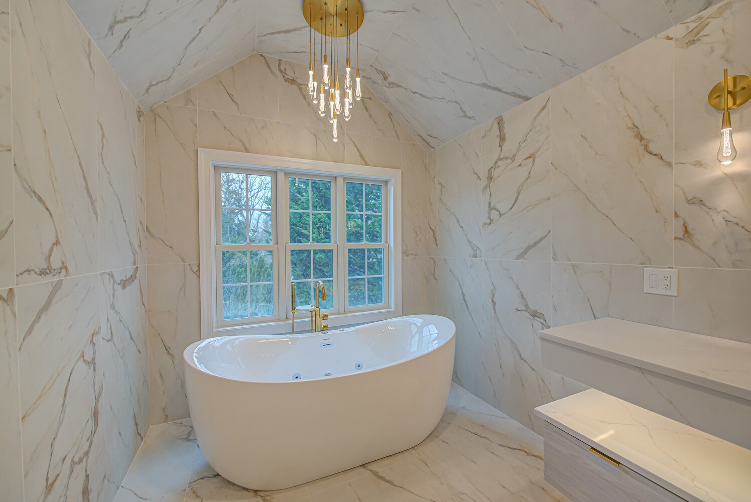Spa-like freestanding bathtub set beneath modern chandelier in custom bathroom by Long Island Creative Contracting, Inc. in Huntington, NY