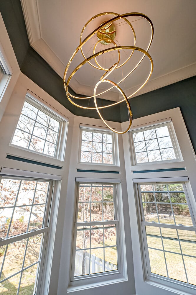 Circular chandelier framed by bay windows in a Poquott, NY home by Long Island Creative Contracting, Inc