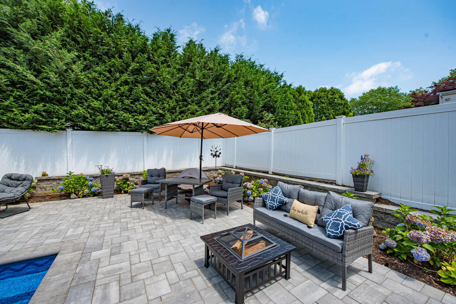 Custom poolside seating area with fire pit and umbrella by Long Island Creative Contracting in Miller Place, NY