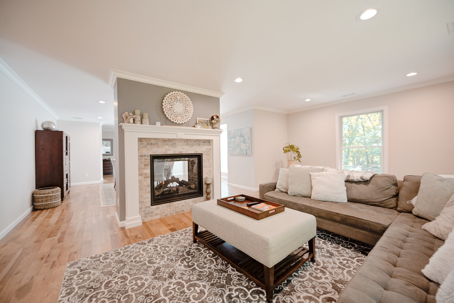 Stylish living room with L-shaped sectional and fireplace in a Port Jefferson custom home by Long Island Creative Contracting, Inc